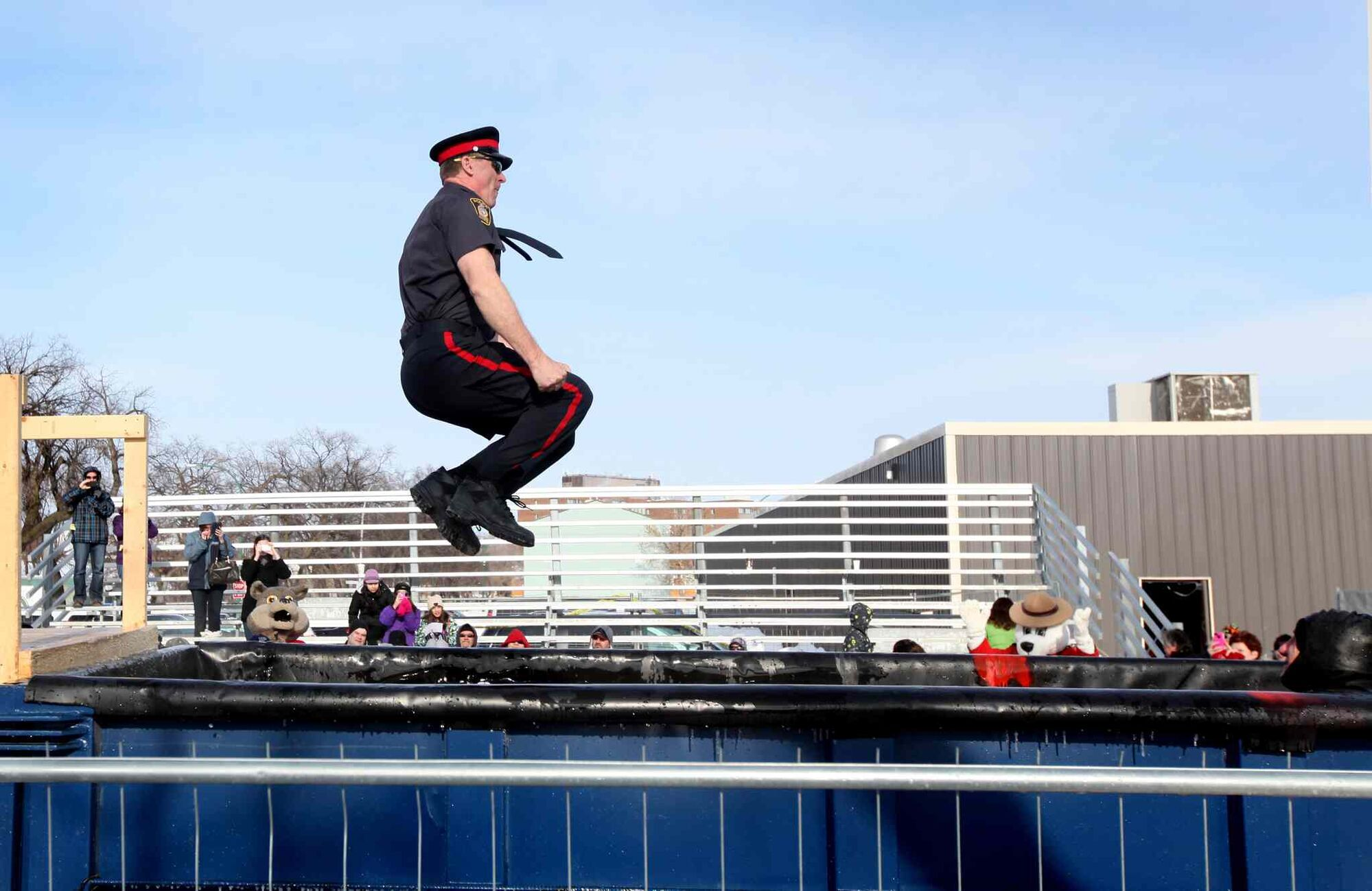 A police officer midair jumping into a pool for a meagre crowd of onlookers