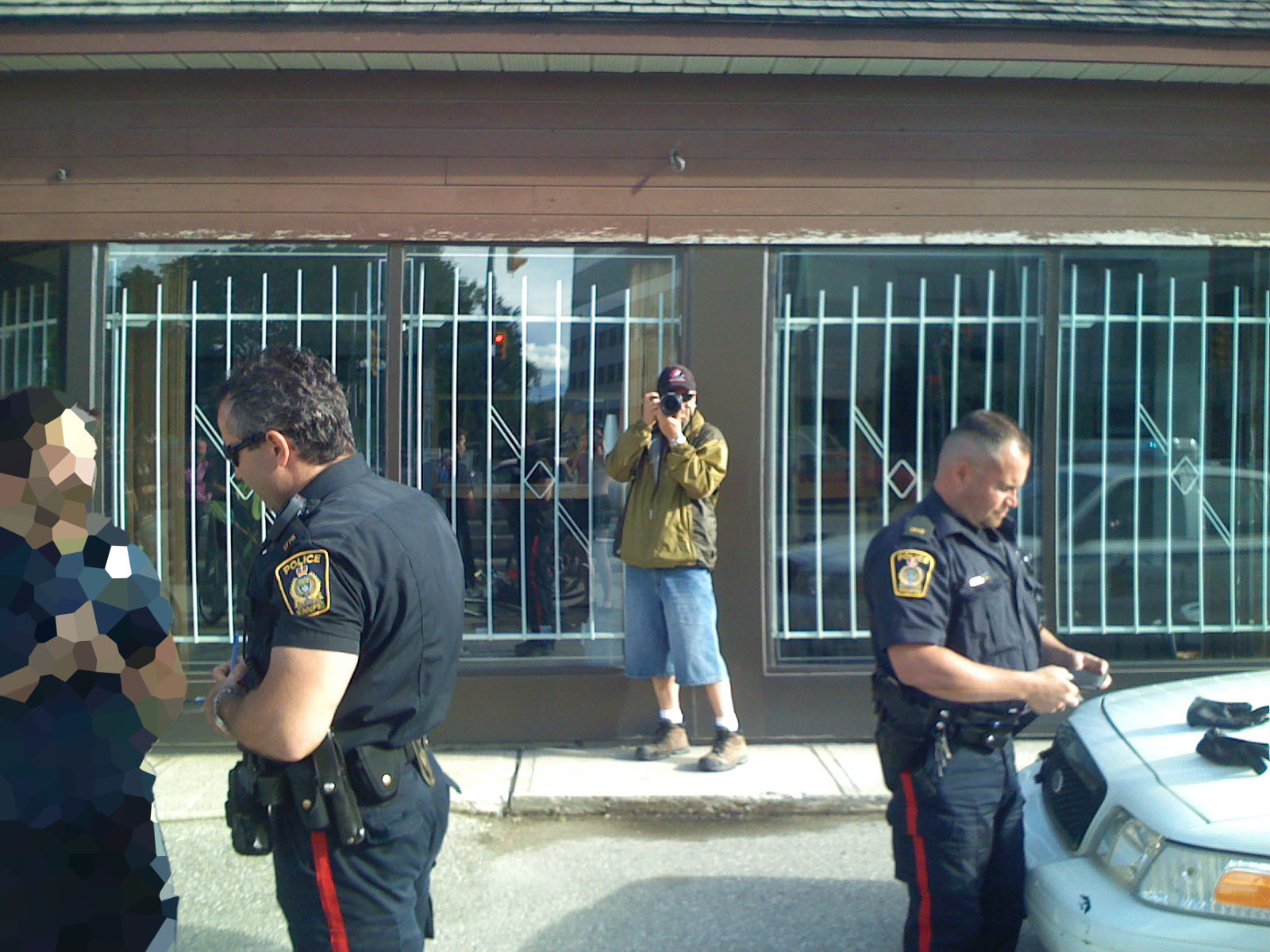 From left to right, a pixelated figure being interrogated by a police officer, a person facing the camera taking a photo, and an officer looking at something with gloves on a police car hood