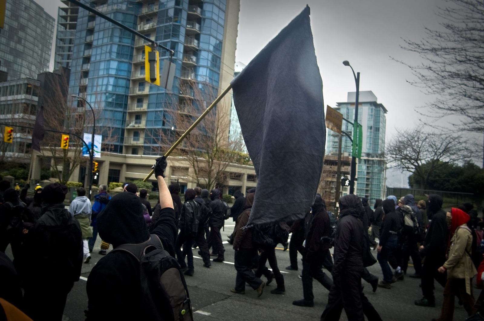 A group in black bloc dress walking laterally across the video, one person waving a large black flag