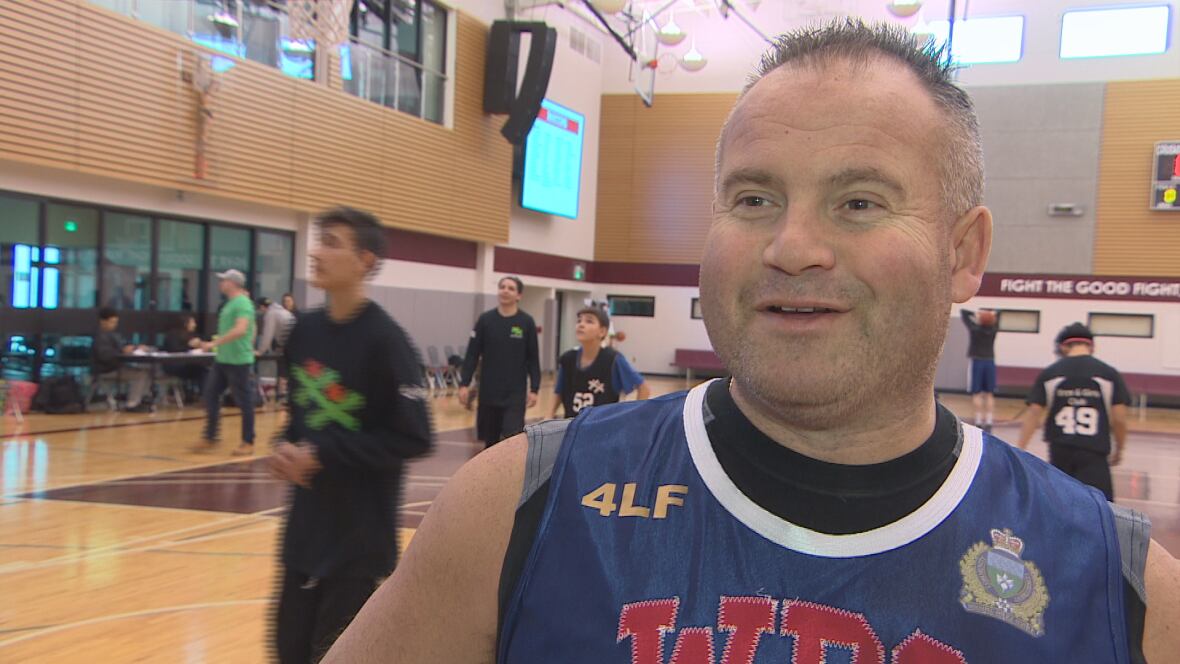 A smiling beefy balding man in a sleeveless Winnipeg Police service jersey at a basketball game